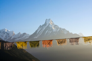 Buddhist prayer flags illuminated by rising sun in front of blurred Machapuchare mountain background in Nepal. View of the Fish Tail Machapuchare from the Tatopani village.