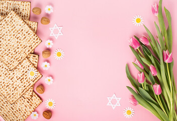 Jewish holiday Passover greeting card concept with matzah, nuts, tulip and daisy flowers on pink background.