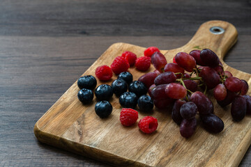 Fresh blueberries, raspberries and grapes on a wooden board