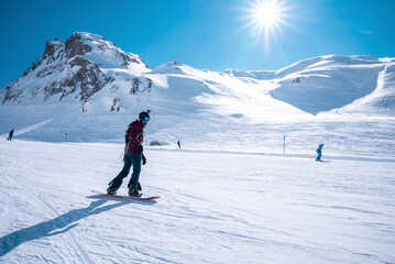Fototapeta na wymiar Young snowboarder sliding down snowy slope on mountain at winter resort
