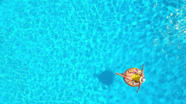 Aerial view of a woman in yellow swimsuit lying on a donut in the pool