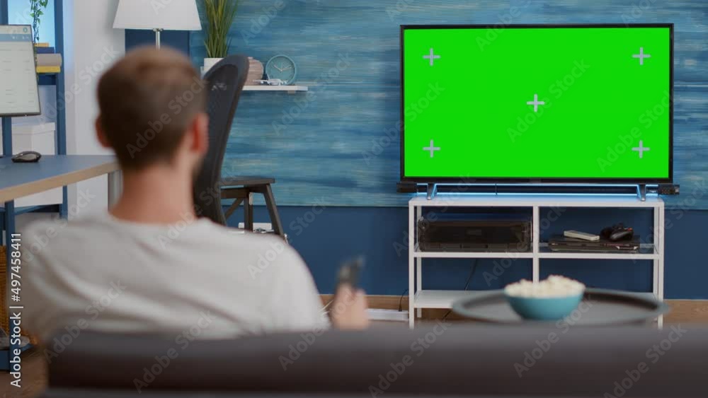 Poster static tripod shot of man switching channels while looking at green screen on tv and sitting on sofa