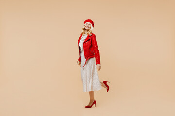 Full size body length fun elderly gray-haired blonde woman lady 40s years old wears red beret jacket dress go move run looking camera smiling isolated on plain pastel beige background studio portrait.