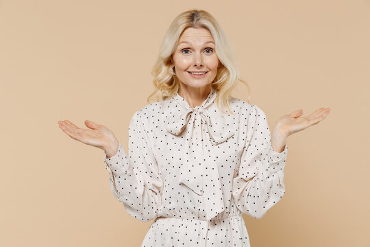 Confused Fascinating Elderly Gray-haired Blonde Woman Lady 40s Years Old Wears Pink Dress Spreading Hands Isolated On Plain Pastel Beige Background Studio Portrait. People Emotions Lifestyle Concept.