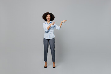 Full body young employee business corporate lawyer woman of African American ethnicity in classic formal shirt work in office point index finger aside on workspace area isolated on grey background