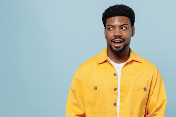 Young amazed fun man of African American ethnicity 20s wear yellow shirt look aside on workspace area mock up isolated on plain pastel light blue background studio portrait. People lifestyle concept.