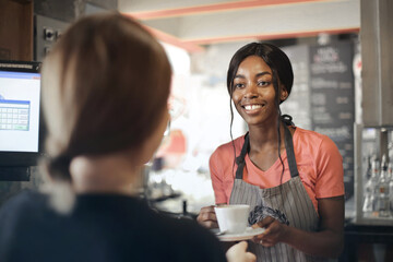 young waitress serves coffee to a customer - Powered by Adobe