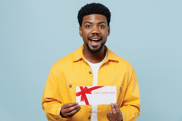 Young shocked man of African American ethnicity 20s in yellow shirt hold gift certificate coupon...