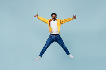 Fototapeta na wymiar Full body young man of African American ethnicity 20s wear yellow shirt jump high with outstretched hands legs isolated on plain pastel light blue background studio portrait. People lifestyle concept.