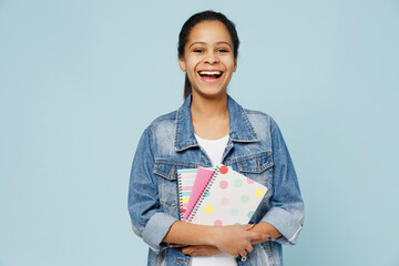 Little smiling fun schoolgirl kid teen girl of African American ethnicity 12-13 years old in denim jacket hold exercisebooks notebooks isolated on pastel plain light blue background Childhood concept