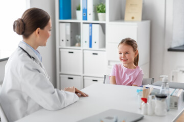 medicine, healthcare and pediatry concept - female doctor or pediatrician talking to happy smiling little girl patient on medical exam at clinic