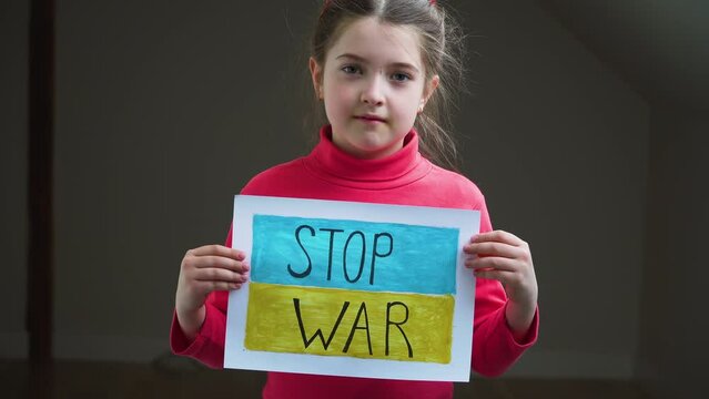 Girl holding self made picture with text Stop war on background of Ukrainian flag in refugee camps. Crisis, peace, stop aggression in whole world
