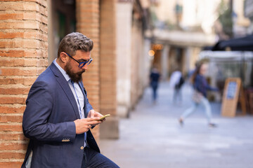 Adult man leaning on column using his phone outside