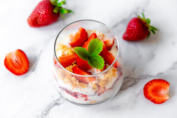 Strawberry dessert with white cocolate, whipped cream, granola and fresh strawberry in individual trifles glass on marble. Recipe of simple healthy homemade organic dessert, cheesecake, parfait.