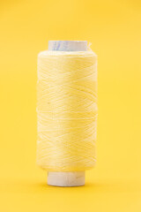 single cream color yarn or spool thread over on yellow background