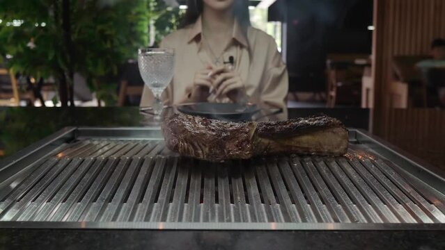 Turning a tomahawk steak. A chef in black gloves prepares an exquisite piece of grilled meat in front of a customer in a restaurant. Rare juicy beef. Smoke from the barbecue. Unrecognizable people.