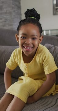 Vertical video portrait of smiling african american girl sitting on couch in living room