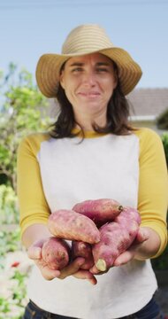 Vertical video of smiling caucasian woman in sunny garden carrying freshly harvested beets