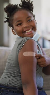 Vertical video of smiling african american girl showing plaster on arm after coronavirus vaccine