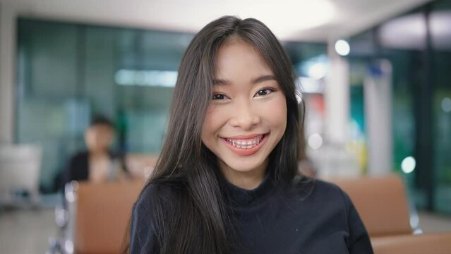 Attractive Asian female traveller smile looking at camera while waiting for her flight at airport terminal. travel idea concept.
