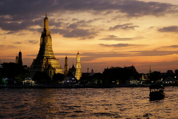 The sun sets near the Wat Arun Buddhist temple located in the bank of Chao Phraya river, Bangkok, Thailand.