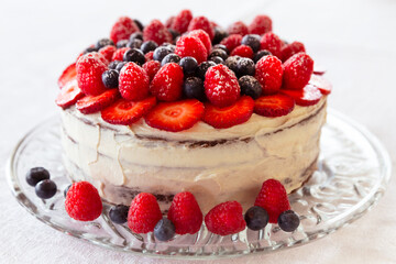 A chocolate and cream naked cake with strawberries, blueberries and raspberries against a white background.