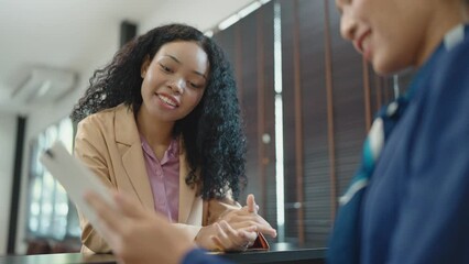 Smiling receptionist giving hotel information service to female guest upon arrival. African black woman guest booking tour at hotel.