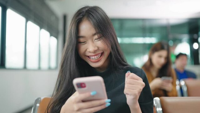 Happy Asian woman using phone celebrating success online win, girl reading good news, in gate at airport.