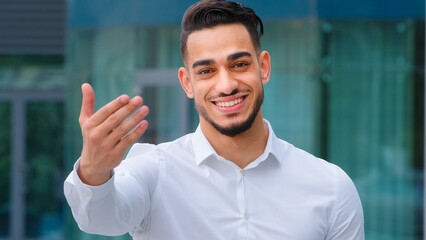 Portrait friendly smiling toothy hispanic arab business man spaniard boss wears white formal shirt showing gesture of invitation advice to approach with hand asks to come outdoors, body languages sign - obrazy, fototapety, plakaty
