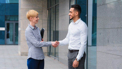 Two multiethnic colleagues arab man and caucasian woman business partners handshaking outdoors near...