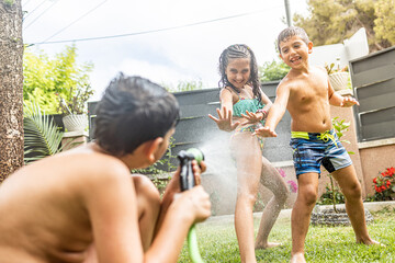 Three funny kids playing with a hose in the garden - obrazy, fototapety, plakaty
