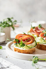 Bruschettas with baguette, bacon or meat, cream cheese, micro-greenery, fresh cucumber and sprouts, in composition on white plate on white textured background