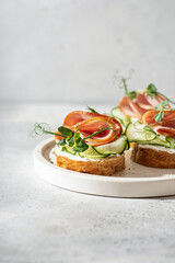 Bruschetta with bread, bacon or meat, cream cheese, micro-greenery, fresh cucumber and sprouts, on white plate on white textured background with text space