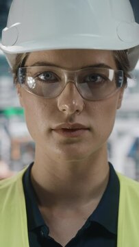 Vertical Portrait of Female Automotive Industry Engineer Putting On Safety Glasses, Wearing High Visibility Vest at Car Factory. Confident Assembly Plant Specialist Working on Manufacturing Vehicles.
