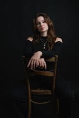 Young lady sitting on chair. Black background. Caucasian. Brunette. Piercing