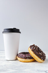 white glass with coffee on a light wooden background with donuts
