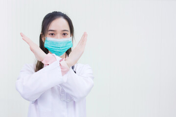 Professional Asian woman doctor wears medical face mask while shows crossed arms in stop sign (stop mark) on white background.