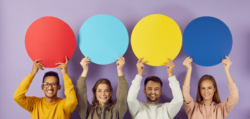 Colored round speech bubbles with copy space in hands of happy young people on purple background....