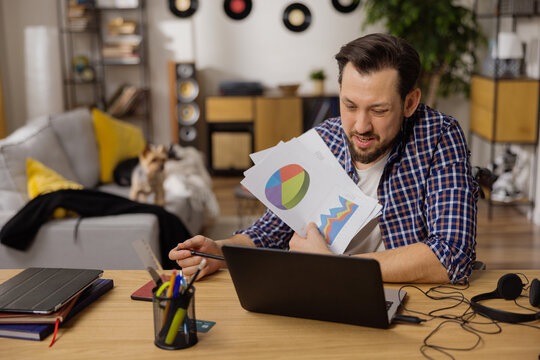 A talking man in a white t-shirt is showing documents towards a laptop. The adult guy is holding a pen with which he is showing different parts of a chart. Video interview.