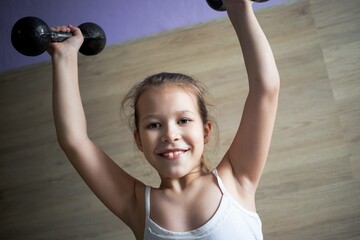 little girl child goes in for sports and poses with two black dumbbells, very hard
