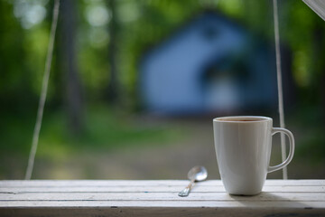 Coffee mug on rail on terrace in garden, blurred home in background, copy space