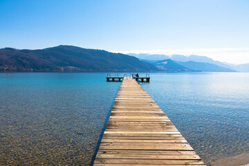 Panoramic view of Lake Attersee with wooden pier and mountain range in the background....