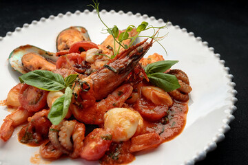 Sauteed seafood on a white plate, on a dark background