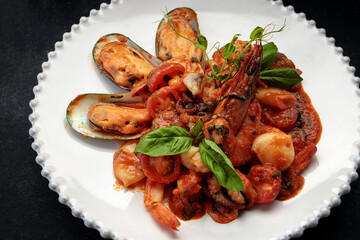 Sauteed seafood on a white plate, on a dark background