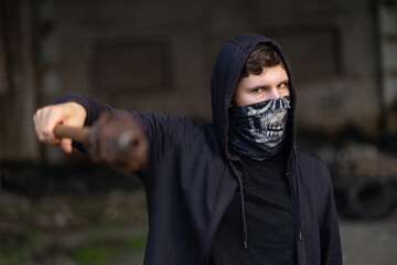 A young tough guy in a buff mask and hood threatens the viewer with a rusty iron bat or a baton...