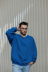Fashionable hipster man with hairstyle and glasses in blue sweatshirt and jeans walks on the street