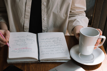 A freelancer girl works in a cafe, drinks cold coffee and makes notes in a notebook with a pink...