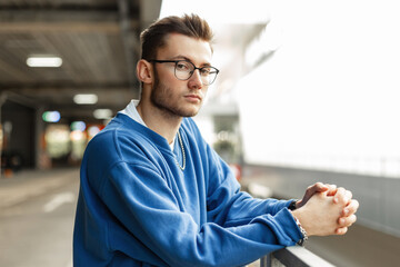 Urban handsome fashion hipster man with glasses and hairstyle in blue stylish classic sweatshirt...
