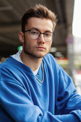 Obraz premium Urban Men's Portrait of a Handsome Hipster Guy with Glasses in a Fashion Blue Sweater in the City
