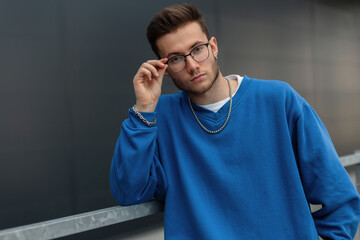 Handsome fashion guy model with hairstyle in blue stylish outfit wears a glasses on the street